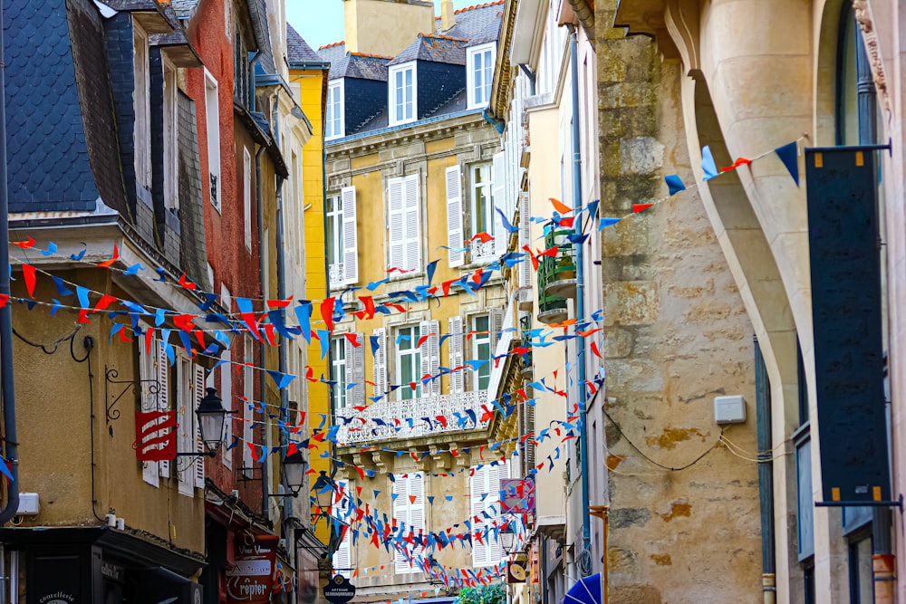 a narrow city street lined with buildings and flags