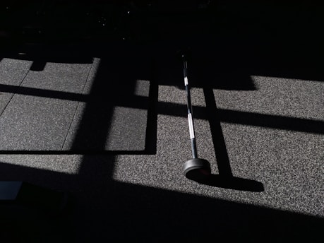 A quiet gym corner bathed in soft morning light, with a lone dumbbell resting on the floor.