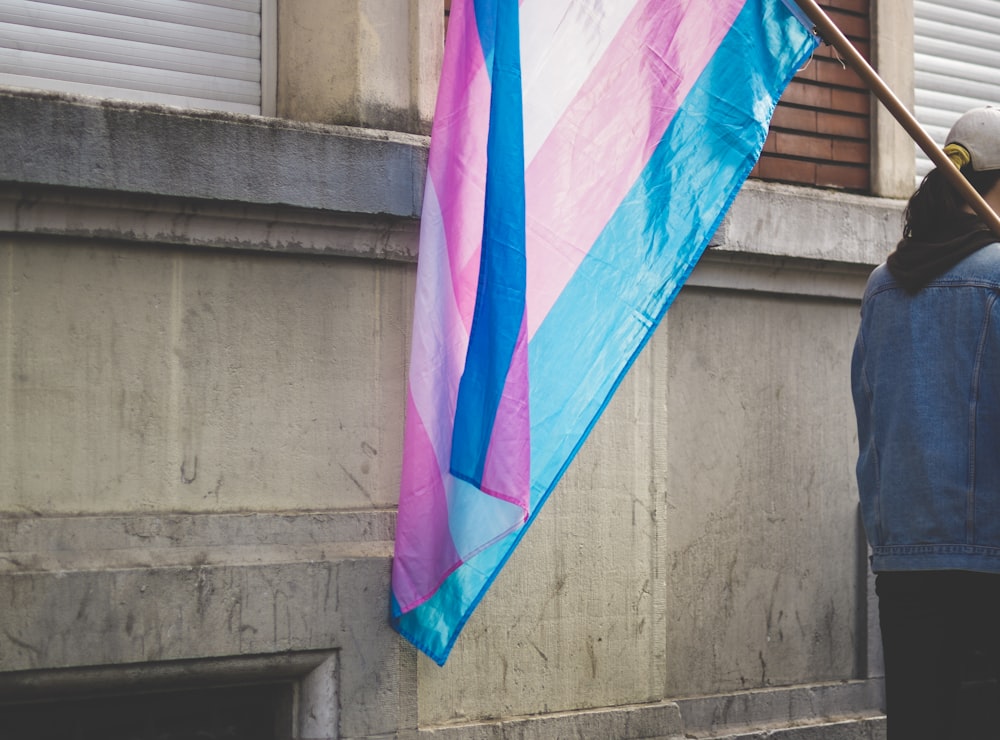 a person holding a pink and blue flag next to a building