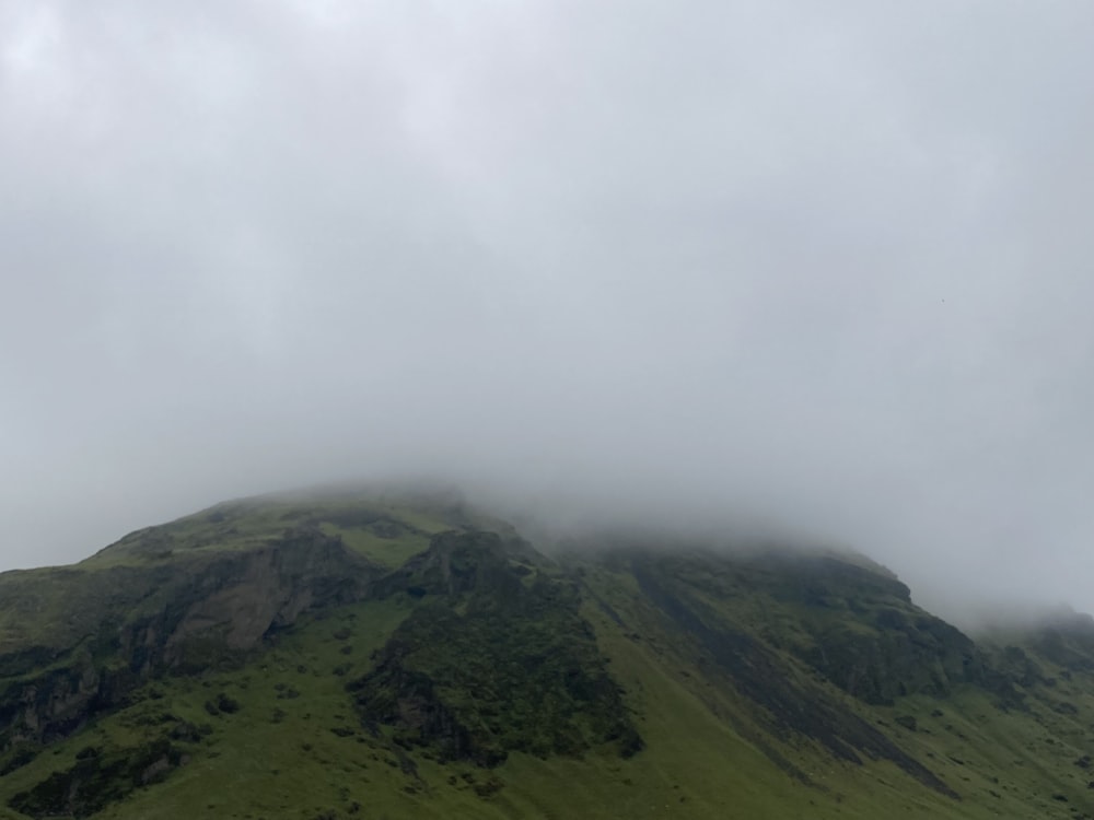a large green mountain covered in clouds on a cloudy day