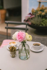 Cozy café table set with coffee, pastries, and a small bouquet of flowers.