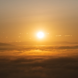 A bright yellow sun rising over mist-covered mountains with a clear blue sky.
