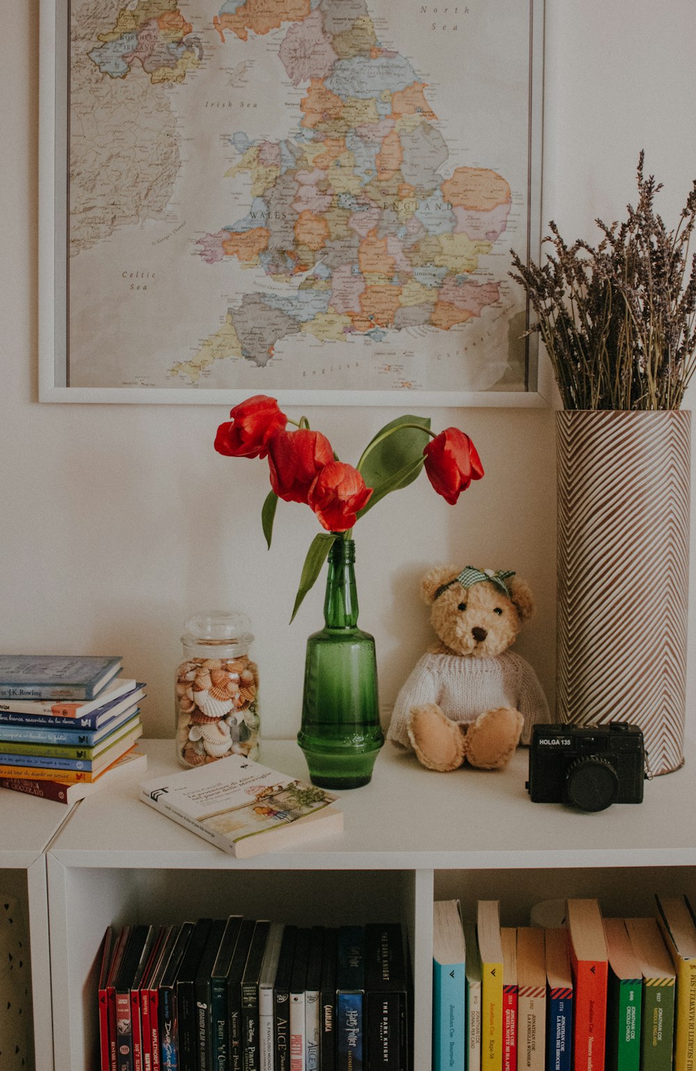 a teddy bear sitting on a book shelf next to a vase with flowers