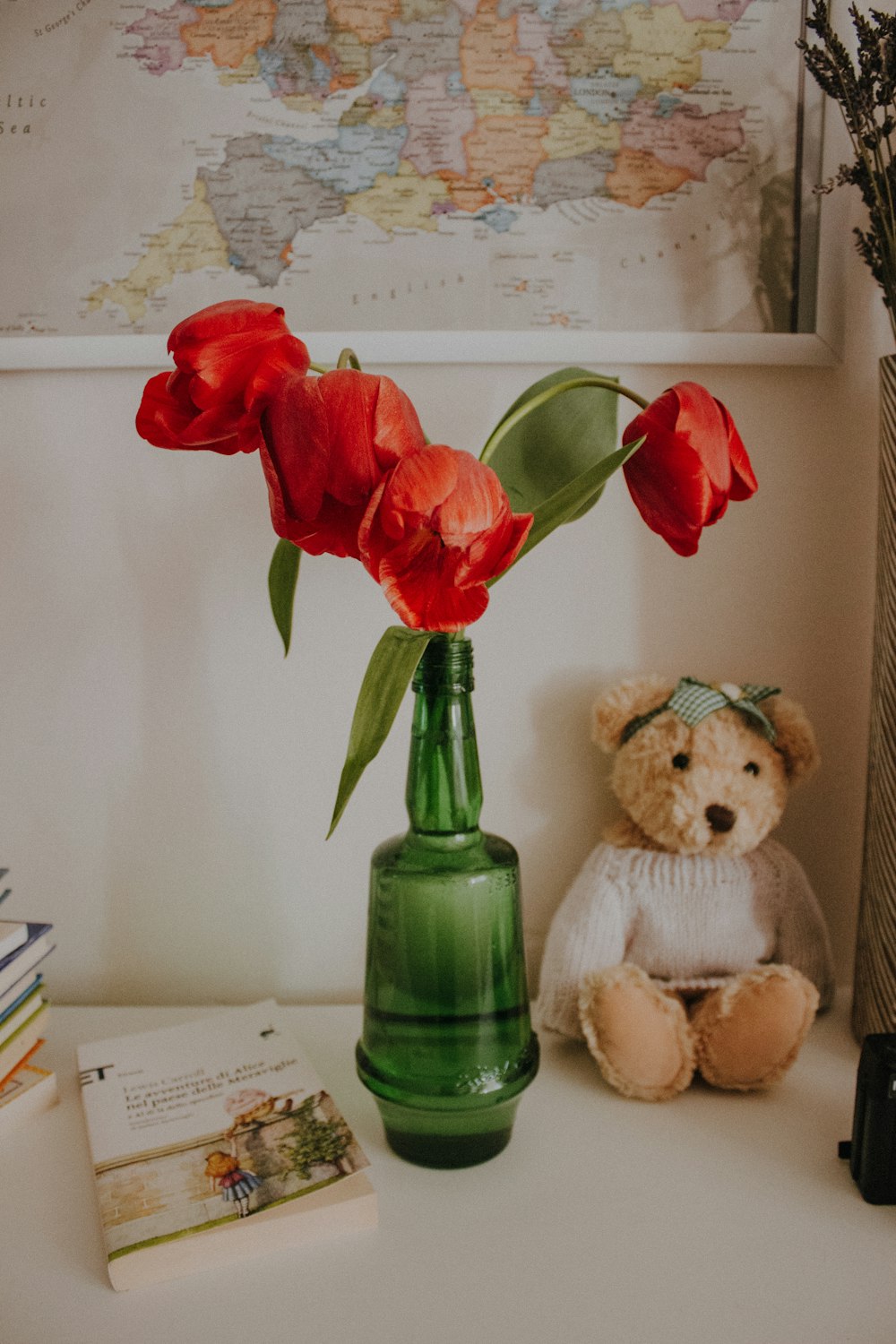 a teddy bear sitting next to a green vase with red flowers