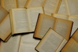 A collection of old, open books with visible text on each page, arranged in an overlapping pattern. The books vary in size and color, with pages showing signs of aging such as yellowing and slight wear around the edges.