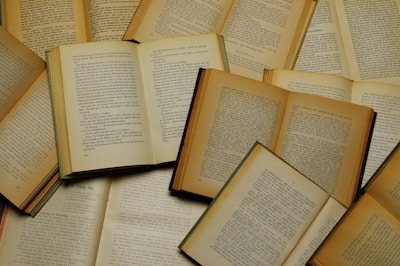 A collection of old, open books with visible text on each page, arranged in an overlapping pattern. The books vary in size and color, with pages showing signs of aging such as yellowing and slight wear around the edges.