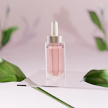 Elegant serum bottle with a dropper surrounded by fresh green herbs and soft pink petals.