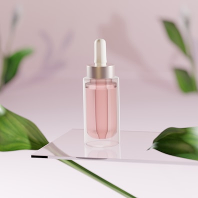 A clear glass dropper bottle containing a pink liquid is positioned on a reflective surface. The background is softly blurred with a pink hue and features green leaves that frame the scene, adding a natural element.