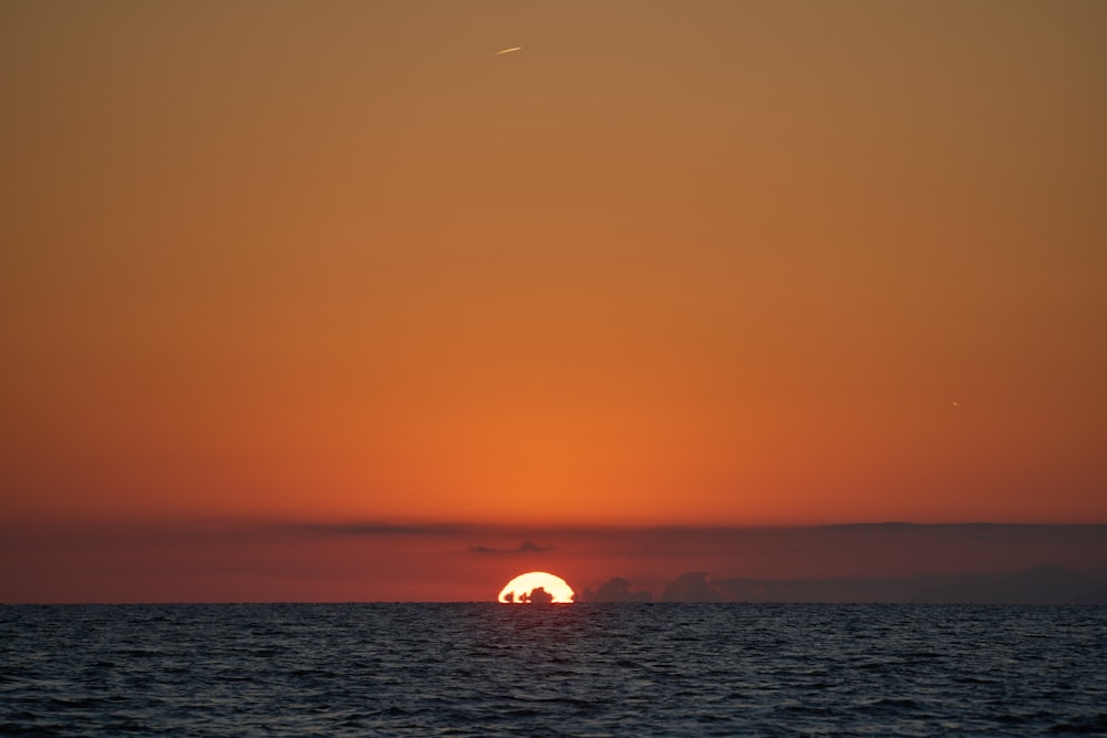 the sun is setting over the ocean with a boat in the water
