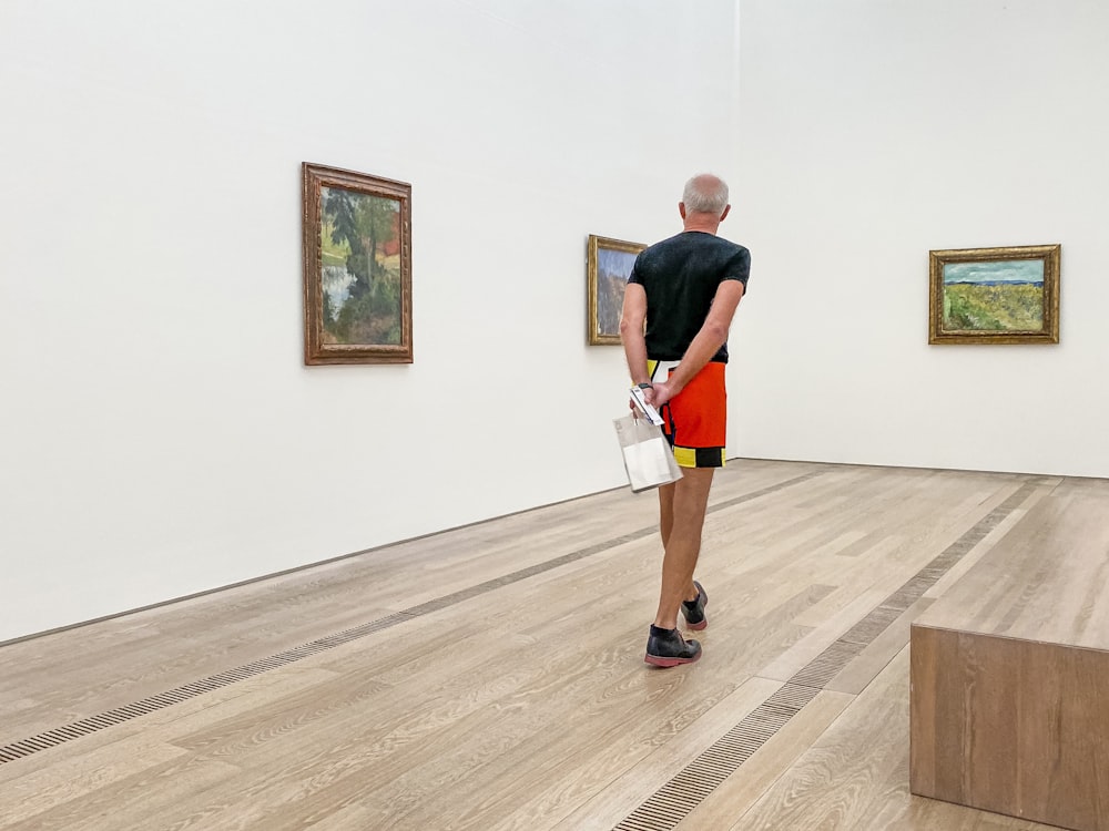 a man standing in an art gallery looking at paintings