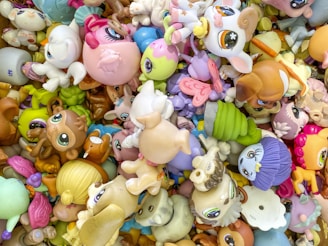 A colorful assortment of toy animals and cartoon characters, featuring large eyes and exaggerated facial features. The toys are piled together in various orientations, creating a chaotic yet vibrant scene.