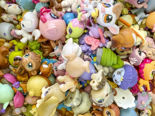 A colorful assortment of toy animals and cartoon characters, featuring large eyes and exaggerated facial features. The toys are piled together in various orientations, creating a chaotic yet vibrant scene.