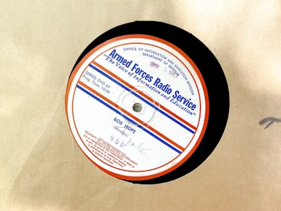 A vintage vinyl record from the Armed Forces Radio Service, featuring a label with text and logos. The label is circular with a red outer rim, a blue line, and several inscriptions including the name 'Bob Hope' and program details. The background is a plain beige surface.