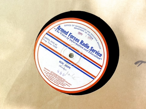 A vintage vinyl record from the Armed Forces Radio Service, featuring a label with text and logos. The label is circular with a red outer rim, a blue line, and several inscriptions including the name 'Bob Hope' and program details. The background is a plain beige surface.