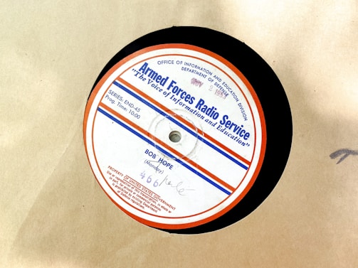 A vintage vinyl record from the Armed Forces Radio Service, featuring a label with text and logos. The label is circular with a red outer rim, a blue line, and several inscriptions including the name 'Bob Hope' and program details. The background is a plain beige surface.