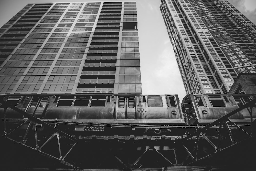 Una foto in bianco e nero di un treno che passa da edifici alti