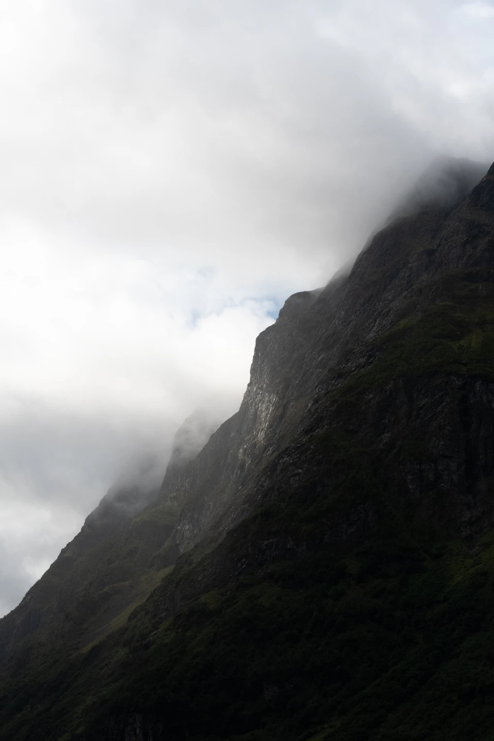 Mountain range with steep rocky cliff face rises into the sky amidst dense foliage