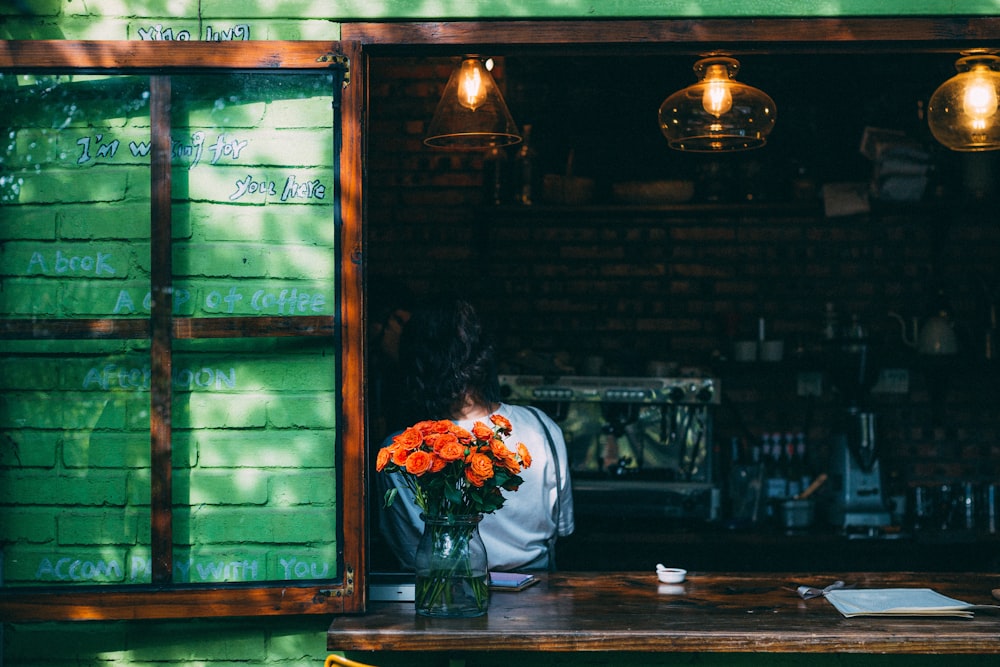 a woman sitting at a table with flowers in a vase