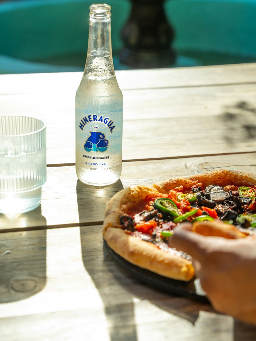 水のボトルの隣の木のテーブルの上に座っているピザ