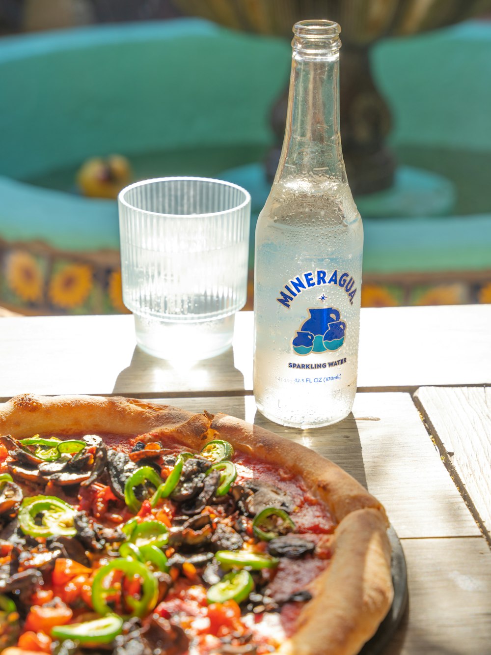 a pizza sitting on top of a wooden table next to a bottle of water