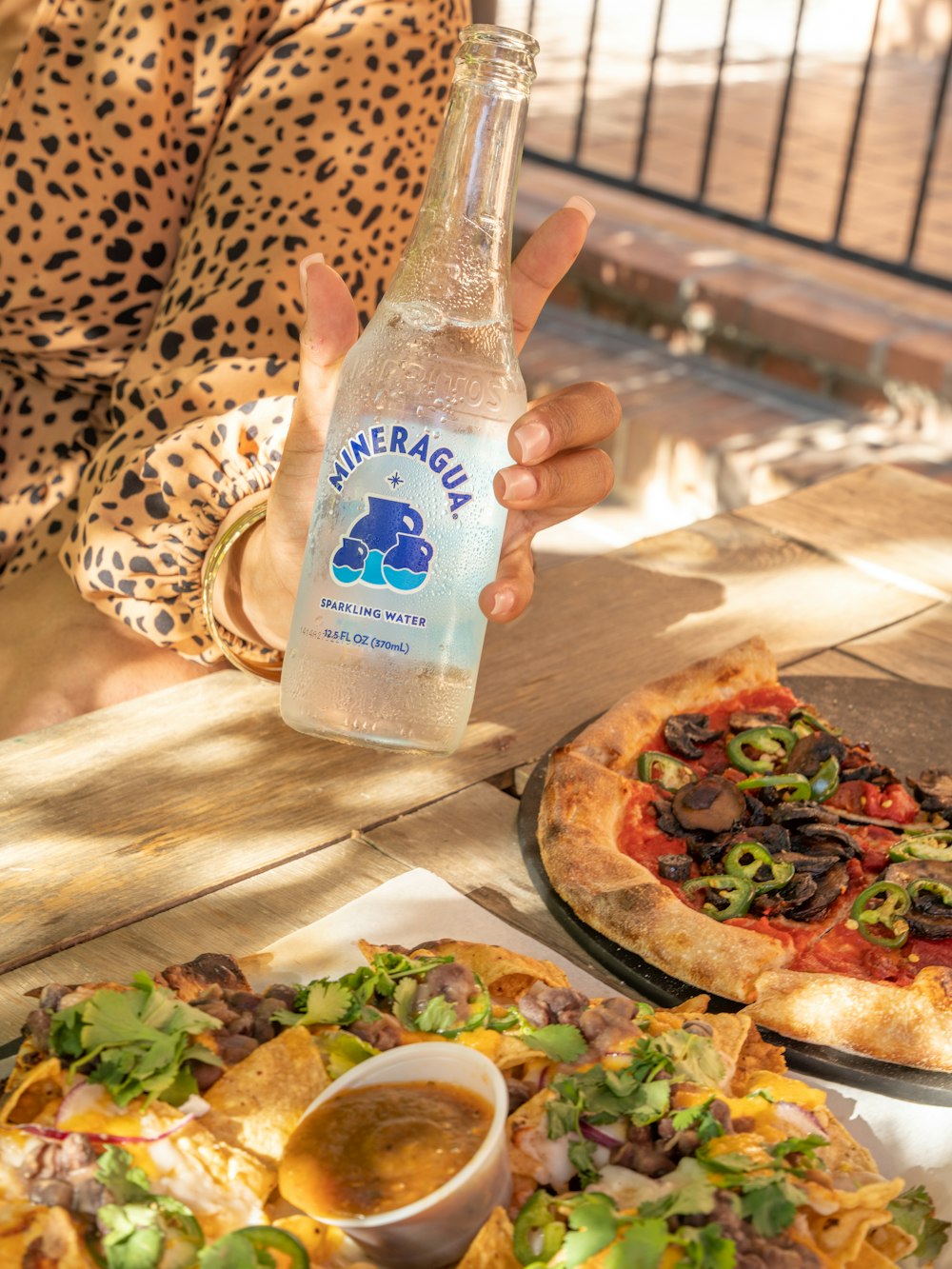 a person holding a bottle of water over a pizza