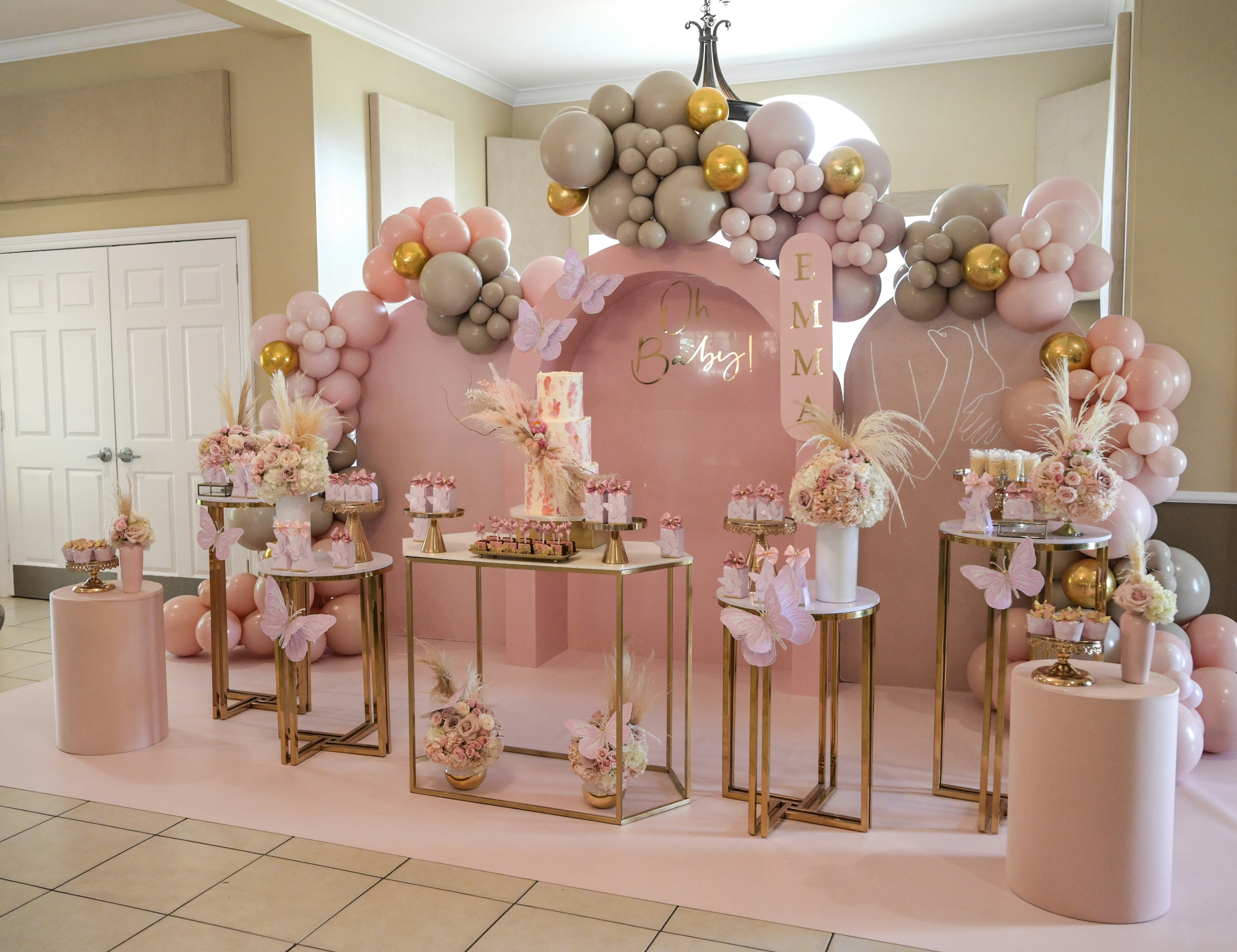 Baby shower table with pastel pink and white balloon garland, floral arrangements, and dessert spread