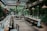 A beautifully set dining area with long tables adorned with elegant tableware and floral arrangements. The space is enclosed by glass walls, allowing natural light to illuminate the room. The walls are covered in lush greenery, creating a cozy and inviting atmosphere.