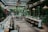 A beautifully set dining area with long tables adorned with elegant tableware and floral arrangements. The space is enclosed by glass walls, allowing natural light to illuminate the room. The walls are covered in lush greenery, creating a cozy and inviting atmosphere.