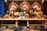 An elaborate and ornate buffet setup featuring a long wooden table adorned with dishes and serving utensils. Behind the table, large decorative golden floral carvings are accentuated by green foliage and white floral arrangements. Ornate candelabras and decorative vases add to the luxurious setup, while the patterned carpet below complements the elegant display.