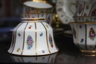 Elegant porcelain teacups and saucers adorned with intricate floral patterns in vibrant colors are displayed. The fine china features gold accents highlighting the exquisite craftsmanship.