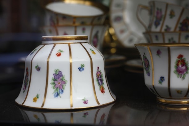 Elegant porcelain teacups and saucers adorned with intricate floral patterns in vibrant colors are displayed. The fine china features gold accents highlighting the exquisite craftsmanship.
