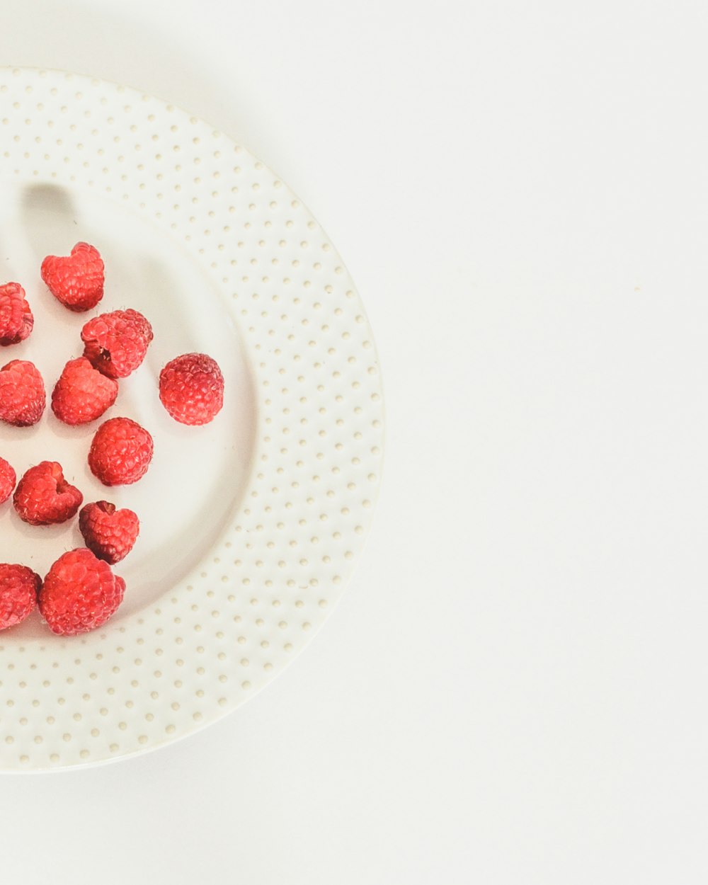 a white plate topped with raspberries on top of a white table