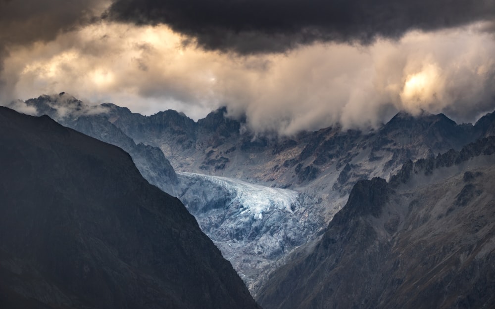 a mountain range covered in snow under a cloudy sky