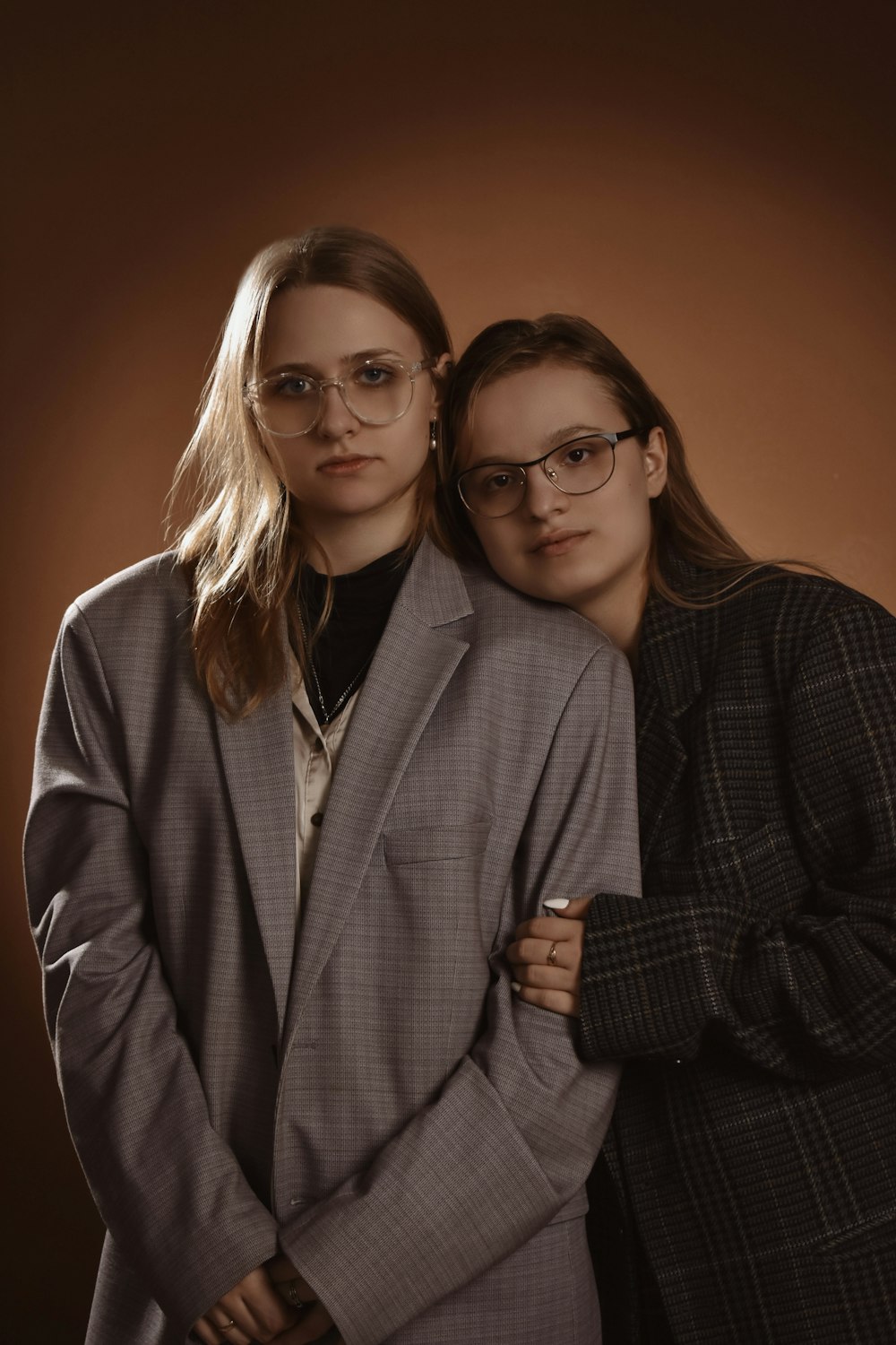 two women standing next to each other in front of a brown background
