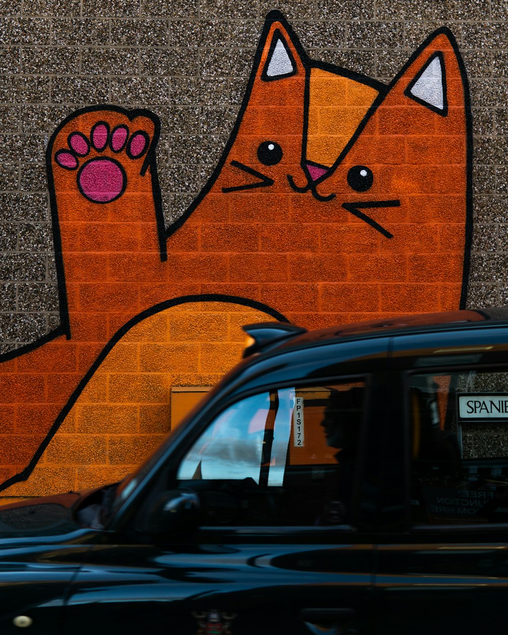 a black car parked in front of a brick wall with a picture of a cat