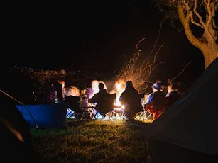 A cozy campsite at dusk with tents, a campfire, and people gathered around.