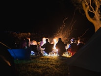 Group of young campers sitting around a campfire sharing stories at dusk.
