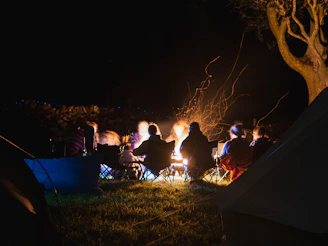 A group of men sitting around a glowing campfire at dusk, sharing stories and laughter.