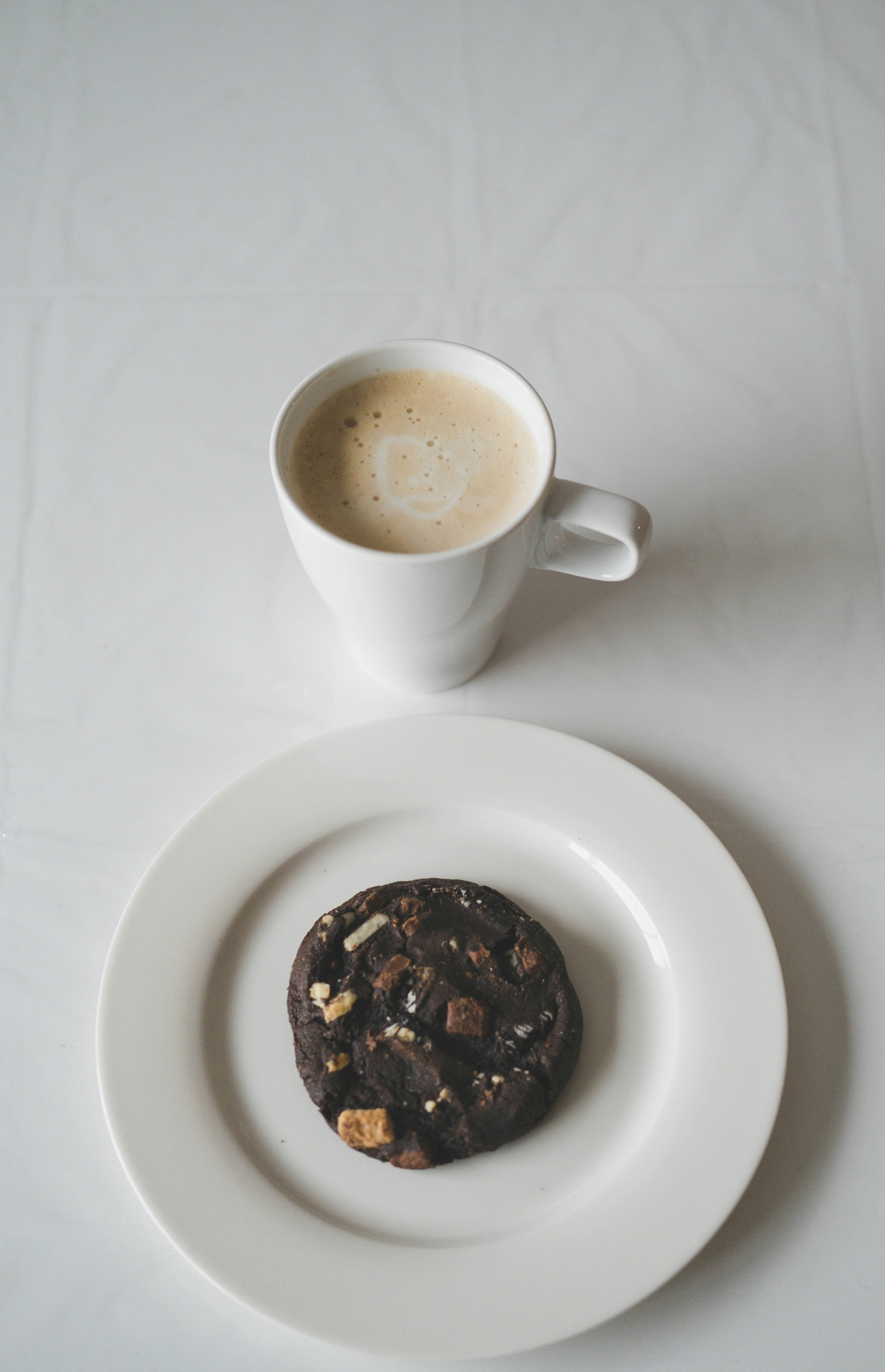 a white plate topped with a chocolate cookie next to a cup of coffee