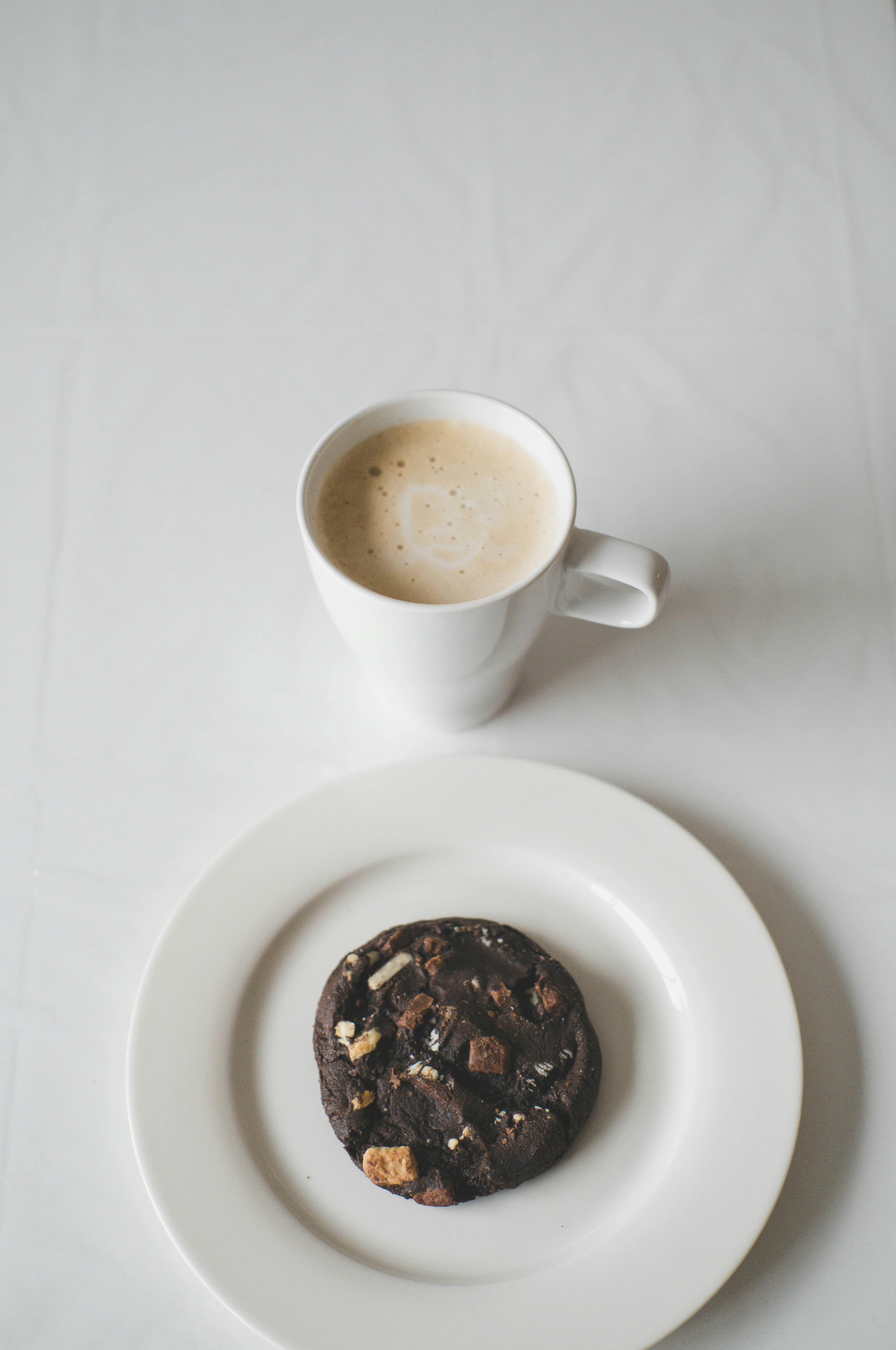 a white plate topped with a chocolate cookie next to a cup of coffee