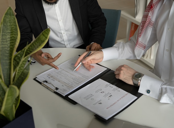 two men sitting at a table with papers and a pen