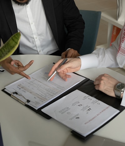 two men sitting at a table with papers and a pen