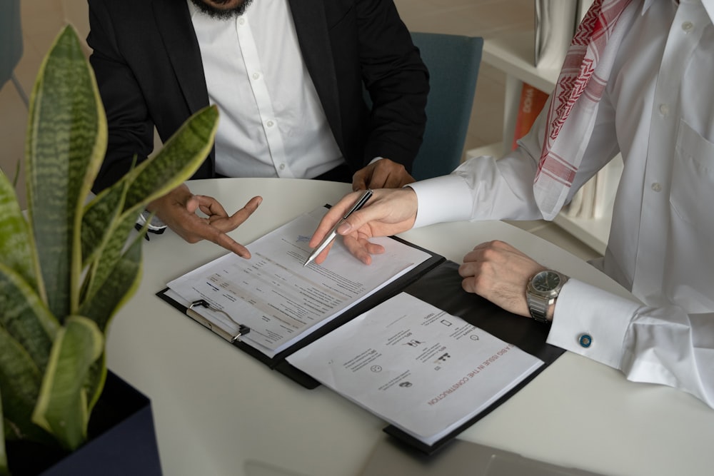 two men sitting at a table with papers and a pen