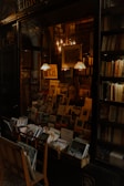 A cozy bookstore display with neatly arranged books and postcards. Warm lighting illuminates the interior, highlighting the vintage decor and a variety of reading materials. Shelves are filled with numerous books and photographs, exuding an inviting and intellectual atmosphere.