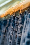 A row of stylish denim jeans hanging on a wooden rack in a bright boutique.