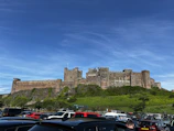 A luxury coach parked outside a historic English castle under a bright blue sky.
