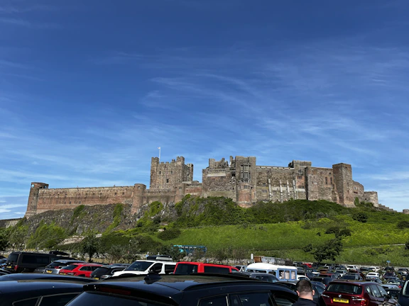 A luxury coach parked outside a historic English castle under a bright blue sky.