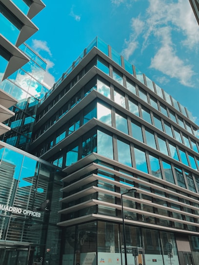 A sleek modern office building facade featuring large architectural glass panels reflecting the blue sky.