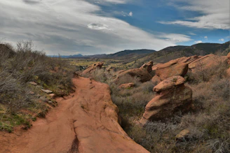 A sunlit red dirt trail winding through the Australian outback with distant rocky hills.