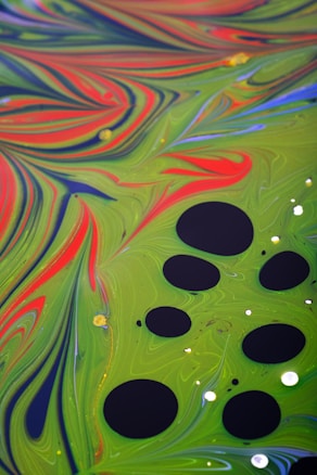 Vibrant abstract design featuring swirling patterns with bold colors, primarily green and red, accented by smooth black circles of varying sizes. Splashes of blue and hints of yellow add contrast, enhancing the dynamic and fluid appearance reminiscent of marbled textures.